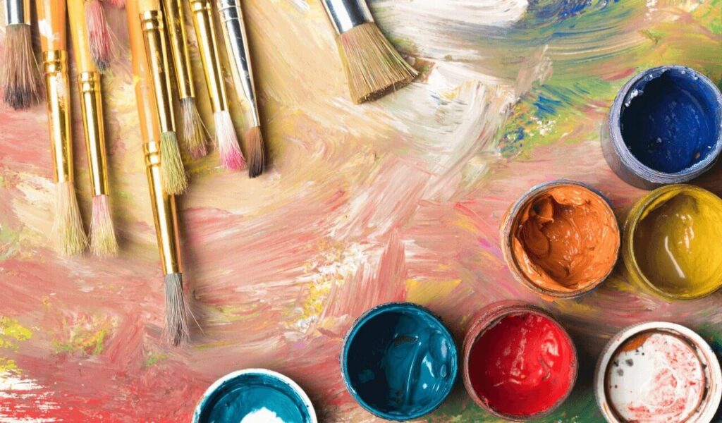 Pinsel und eine mit bunten Farben verschmierte Palette, mit offenen Gläsern herum.