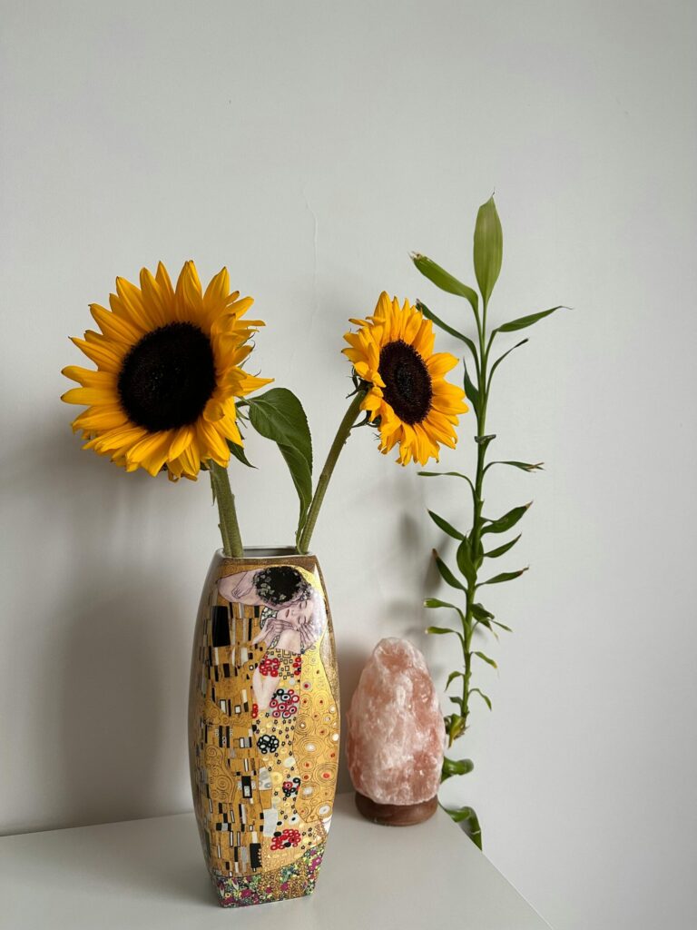Sonnenblumen in einer Klimt-inspirierten Vase mit einer Salzlampe und einer Bambuspflanze im Hintergrund.